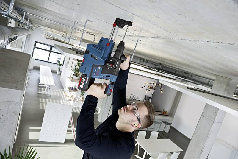 Eine Person bohrt mit einem elektrischen Werkzeug in die Decke eines modern eingerichteten Büros.