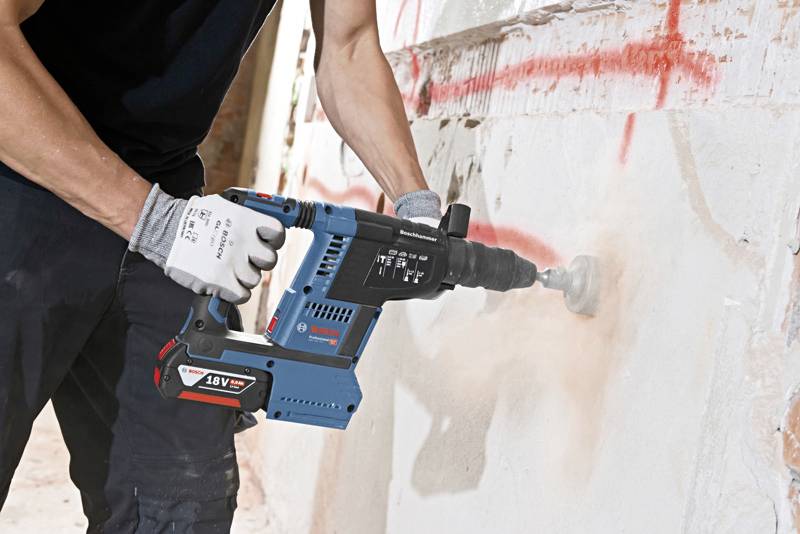 Eine Person bohrt mit einem blauen, kabellosen 18V-Bohrhammer Löcher in eine Wand mit roter Graffiti.