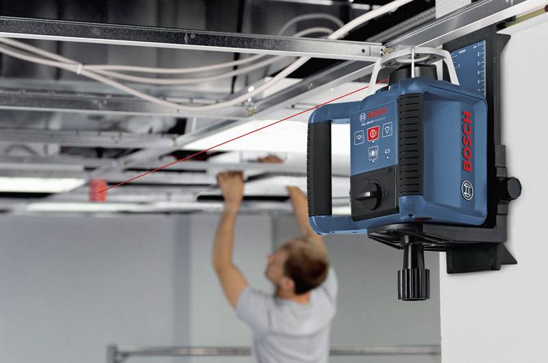 Ein Arbeiter justiert eine Decke mithilfe eines angebrachten Bosch-Lasers zur genauen Ausrichtung, mit sichtbarem roten Laserstrahl.