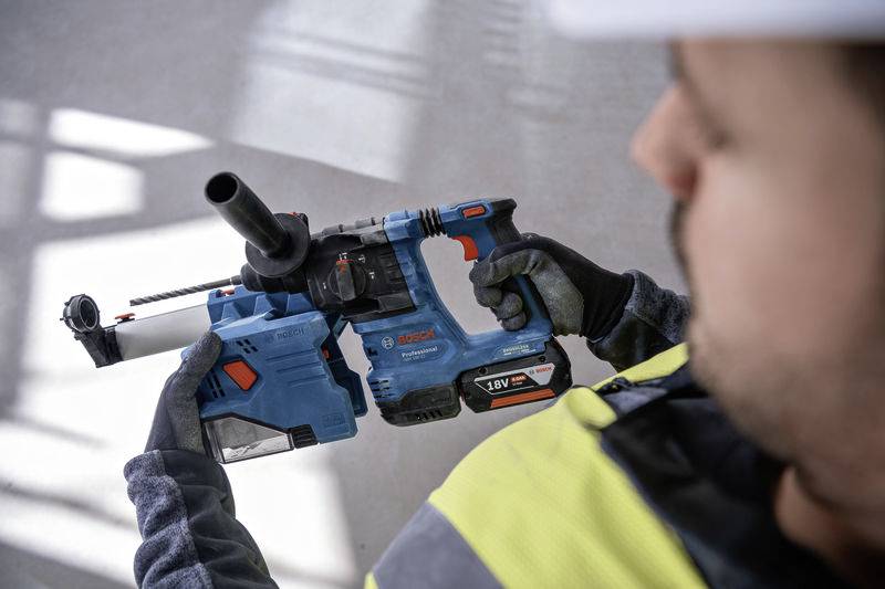 Eine Person hält einen blauen Bohrhammer mit schwarzem Griff. Die Person trägt Sicherheitskleidung, einschließlich Handschuhe und Helm.