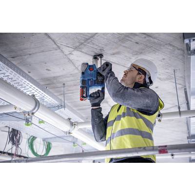 Arbeiter mit Schutzhelm und Warnweste bohrt mit einer Elektrowerkzeugmaschine in die Decke, um Kabel zu installieren.