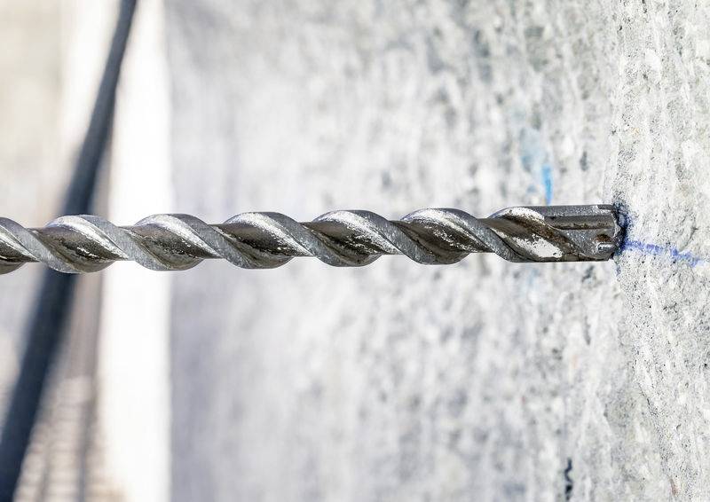 Eine elektrische Bohrmaschine bohrt ein Loch in eine Betonwand. Der Bohrer ist aus Metall, die Wand aus grauem Beton.