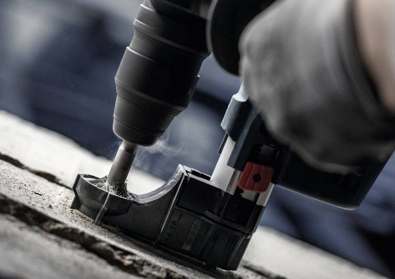 Eine Person verwendet eine Bohrmaschine, um in Beton zu bohren. Staubpartikel sind sichtbar.