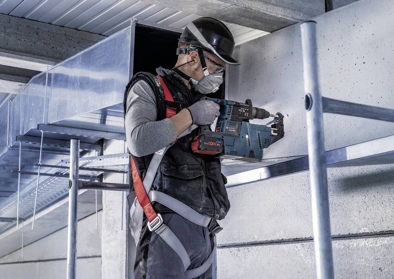 Ein Handwerker in Schutzkleidung und Helm benutzt eine Bohrmaschine, um in eine Metalloberfläche zu bohren.