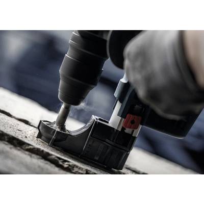 Nahaufnahme eines Bohrers, der in Beton bohrt. Rauch steigt auf, während das Werkzeug arbeitet. Arbeiterhand trägt Schutzhandschuhe.