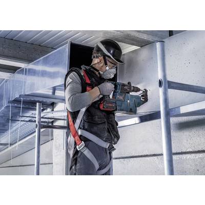 Ein Bauarbeiter trägt Schutzhelm und Maske und bohrt mit einem Elektrowerkzeug in eine Metallkonstruktion in einem Gebäude.