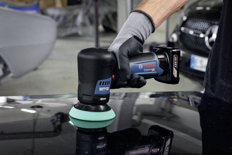 Eine Person poliert mit einem Bosch Akku-Polierer die Motorhaube eines Autos in einer Werkstatt.