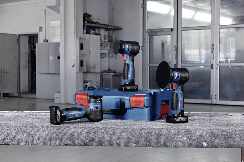 Eine Werkstatt mit zwei blauen Elektrowerkzeugen auf einer grauen Oberfläche, umgeben von Werkzeugkoffern.