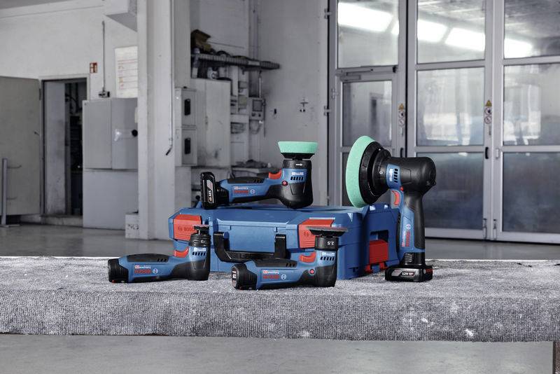 Akkuschrauber und Schleifgeräte auf einem Betonblock vor einer Werkstatt. Markenname auf den Werkzeugen erkennbar. Moderne Umgebung.