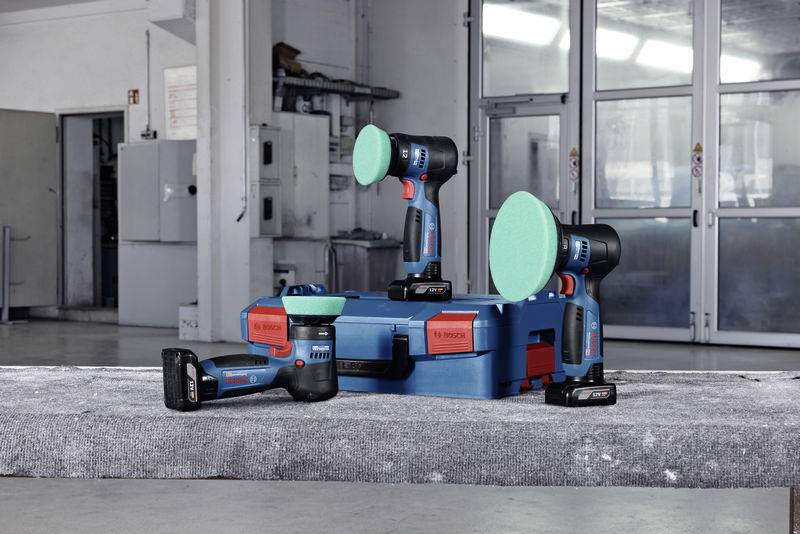 Ein Satz Akkuschrauber und Schleifmaschinen auf einem Tisch in einer Werkstatt mit Koffern und Ladegeräten im Hintergrund.