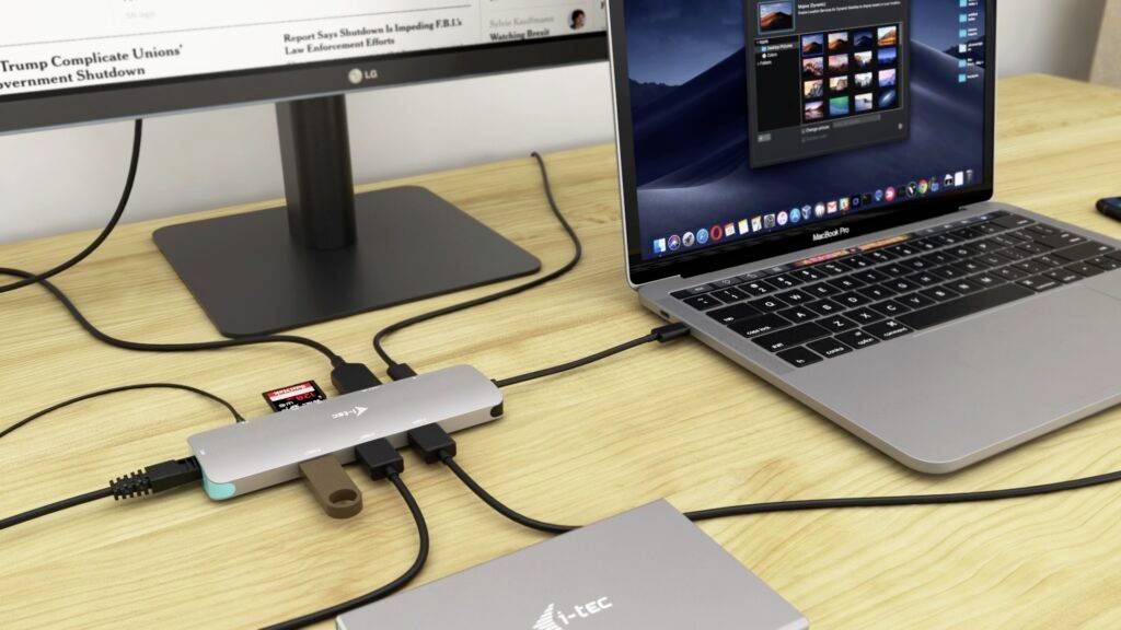 Laptop auf einem Schreibtisch mit mehreren angeschlossenen USB-Geräten und Adaptern, verbunden mit einem externen Monitor.