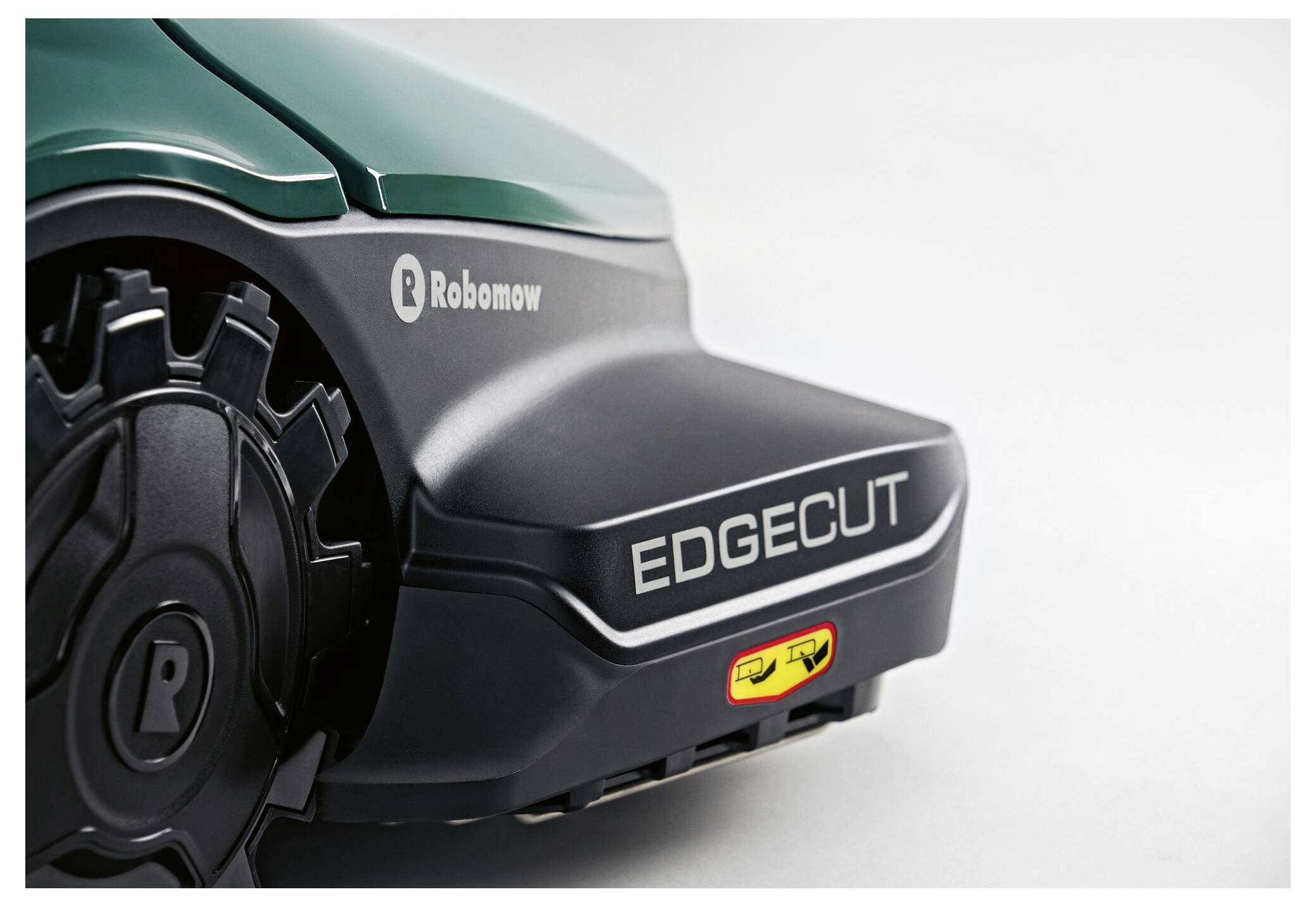 Nahaufnahme eines Rasenmähers mit einem dunkelgrünen Gehäuse. 'Robomow' und 'EDGECUT' sind auf den schwarzen Kunststoffteilen aufgedruckt.