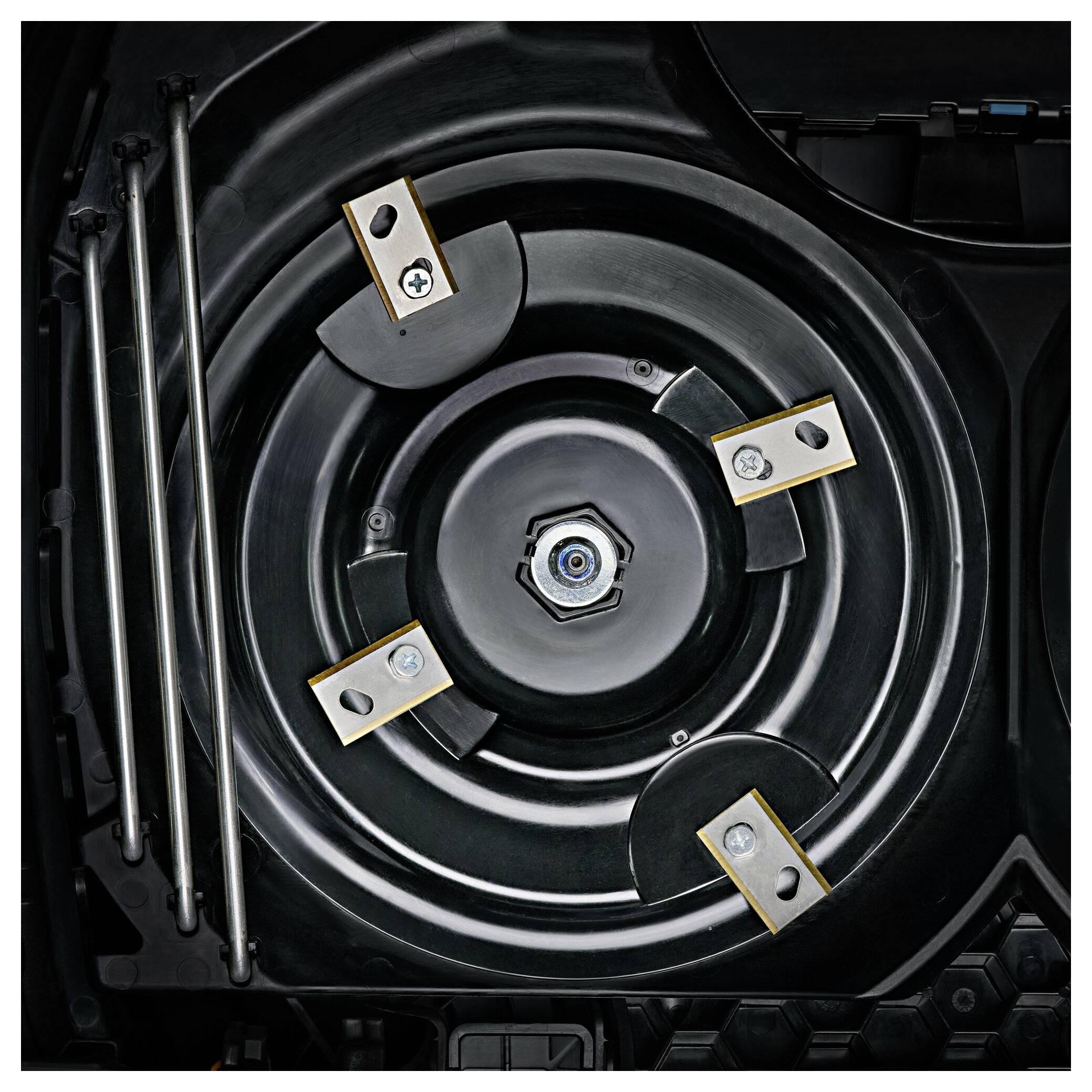 Das Bild zeigt die Unterseite eines Rasenmäherdeckels mit mehreren Klingen und Befestigungen. Links sind drei Metallstangen zu sehen.