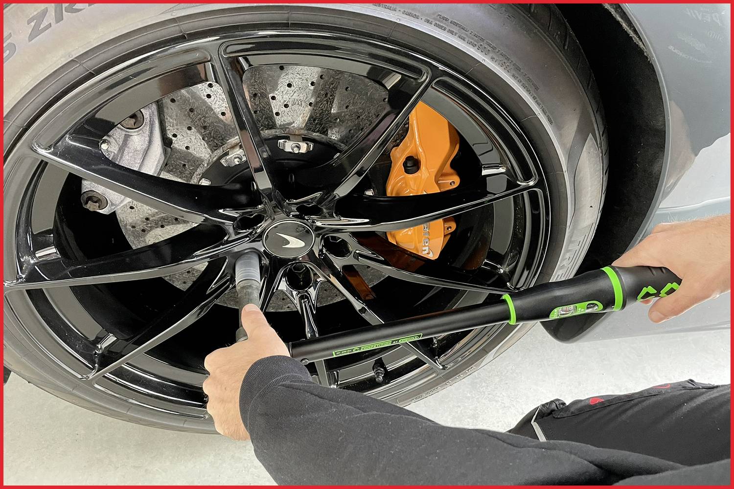 Eine Person zieht mit einem Drehmomentschlüssel die Radmuttern an einem schwarzen Auto mit orangem Bremssattel fest.