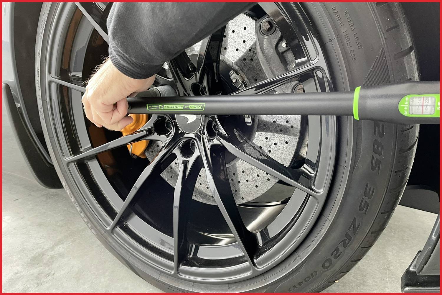Eine Person zieht eine Felgenschraube mit einem Drehmomentschlüssel an einem schwarzen Autoreifen an.