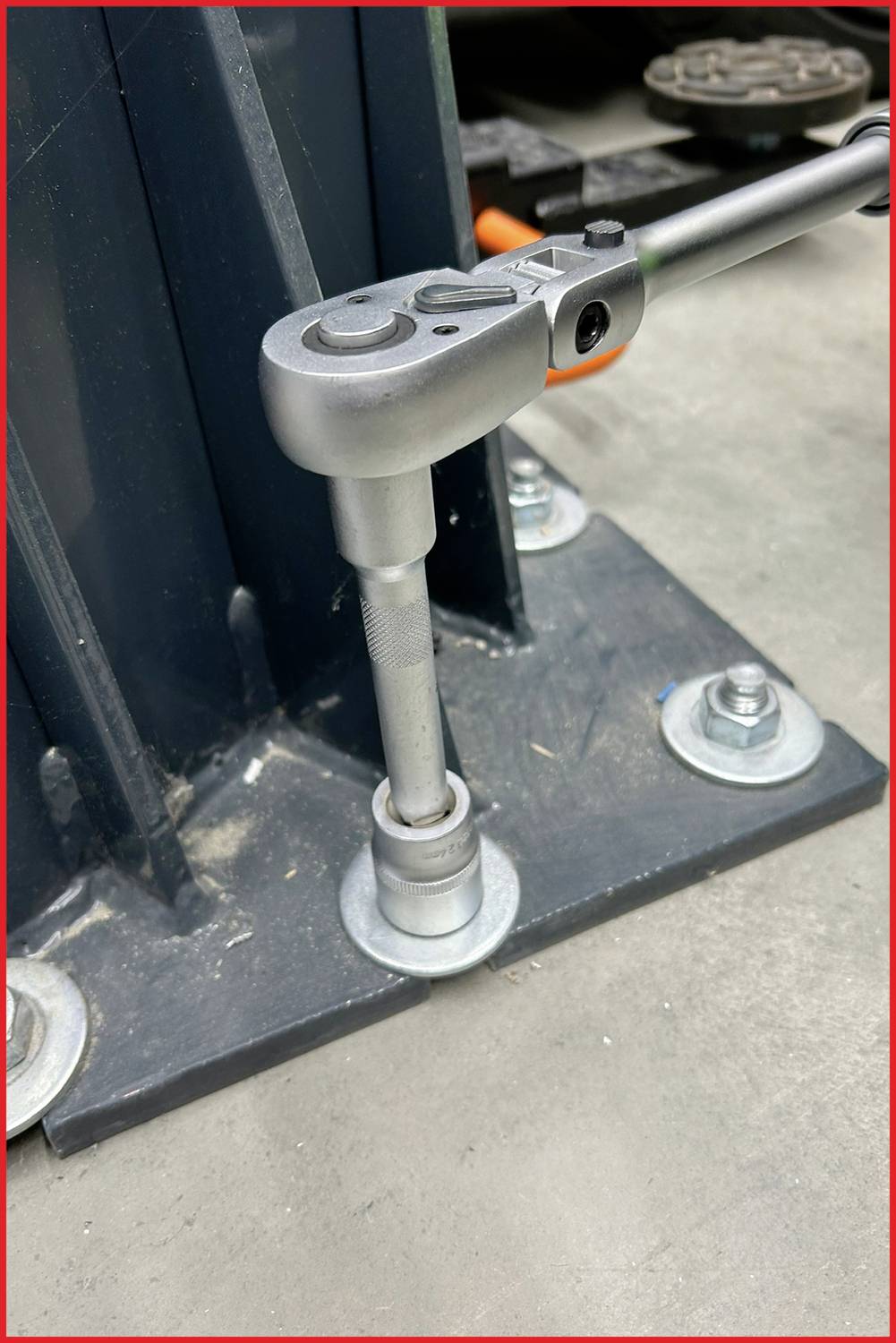 'Umschaltknarre zieht Schraube an, befestigt ein Metallgestell auf Betonboden mit Muttern.'
