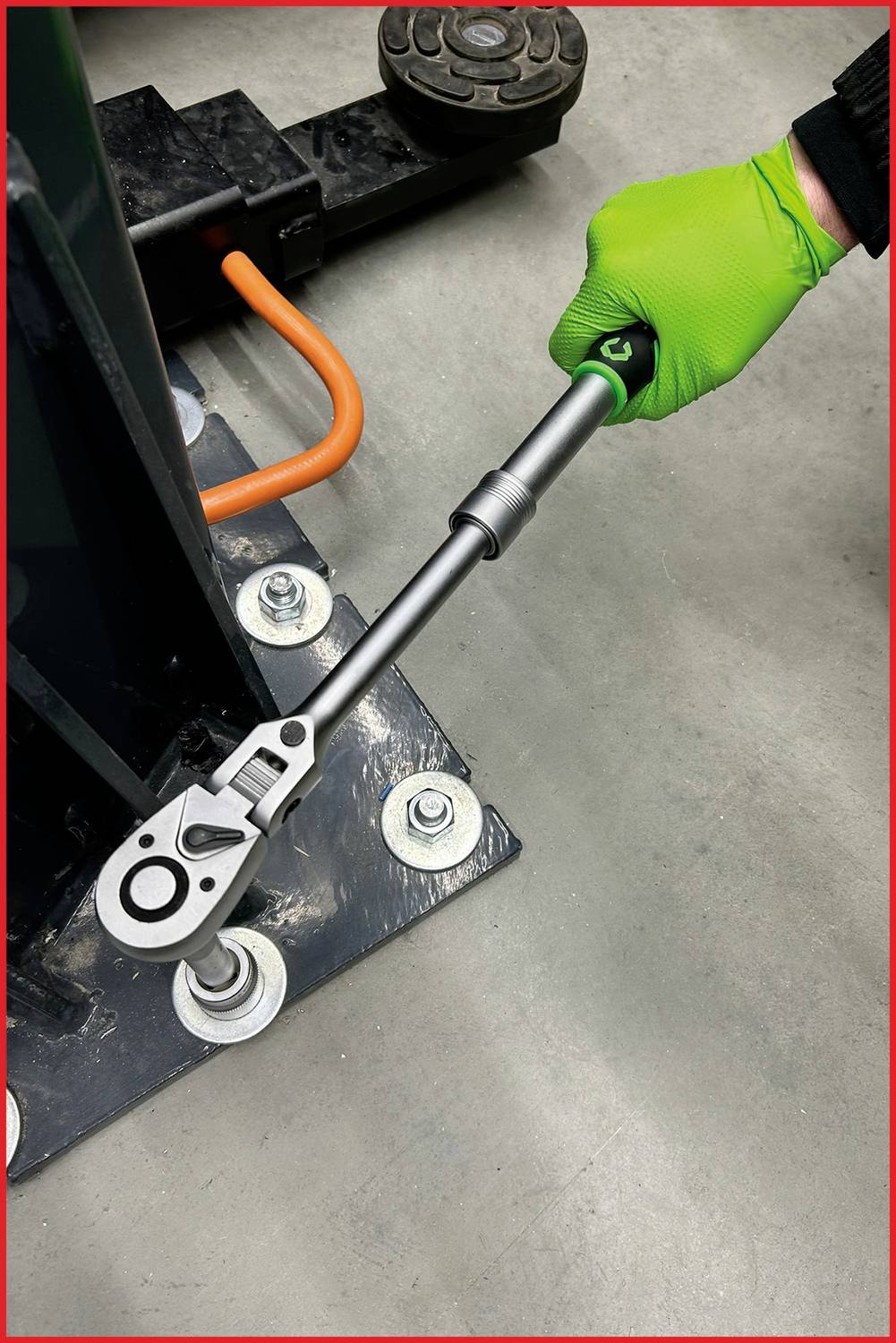 Eine Person mit grünen Handschuhen verwendet einen Drehmomentschlüssel, um eine Schraube an einer Metallstruktur zu befestigen.