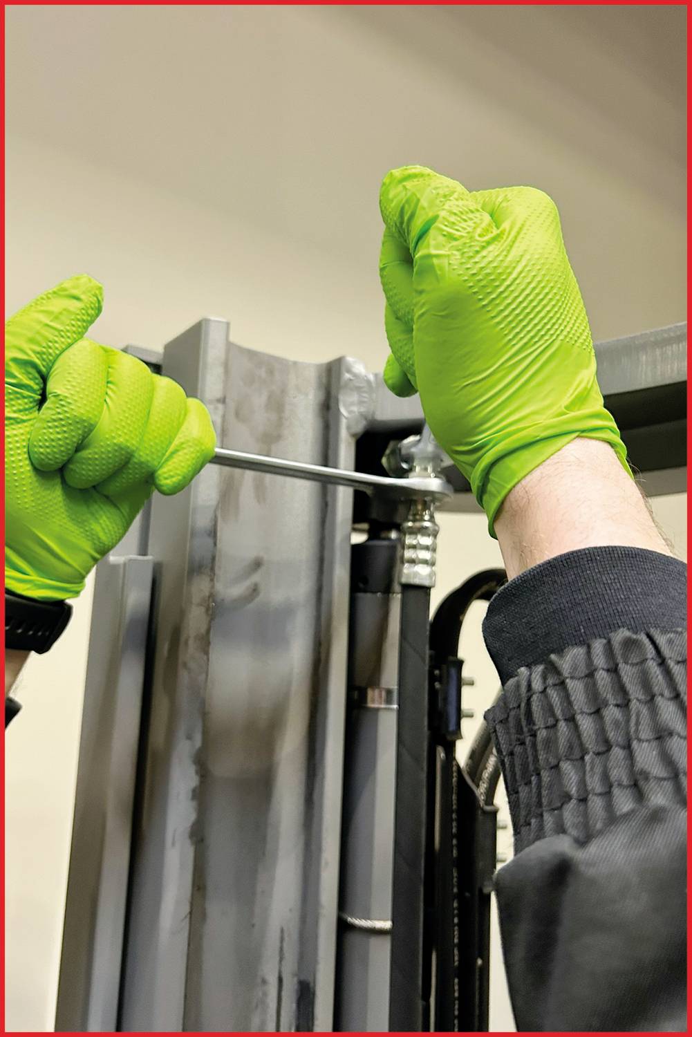Eine Person mit grünen Handschuhen zieht mit einem Schraubenschlüssel an einer Metallvorrichtung.