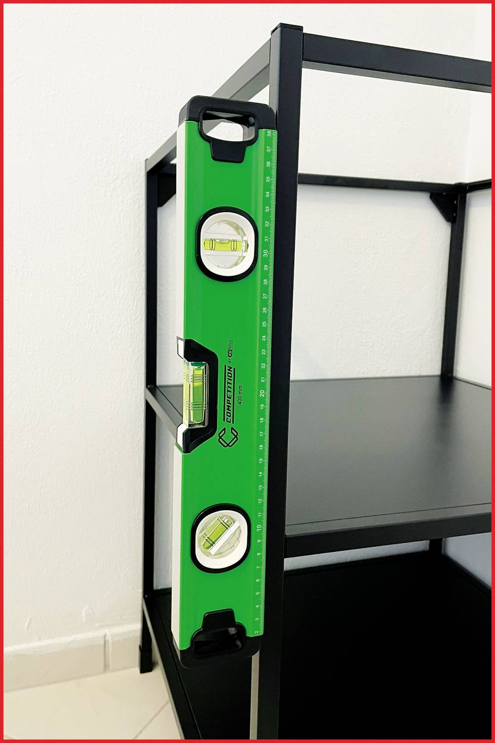 Grünes Lot an schwarzem Regal zur Überprüfung der Ausrichtung. Regal steht auf Fliesenboden an weißer Wand.