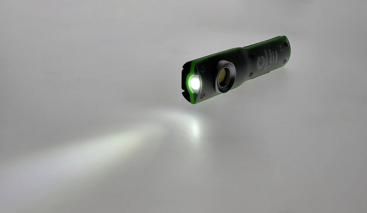 Eine grüne Taschenlampe leuchtet auf eine graue Oberfläche und erzeugt einen Lichtkegel.
