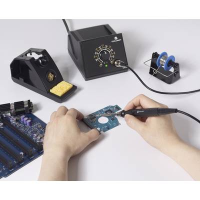 Eine Person, die elektronische Komponenten auf einer Leiterplatte mit einem Lötkolben lötet, wobei eine Lötestation und eine Lötdrahtrolle in der Nähe stehen.