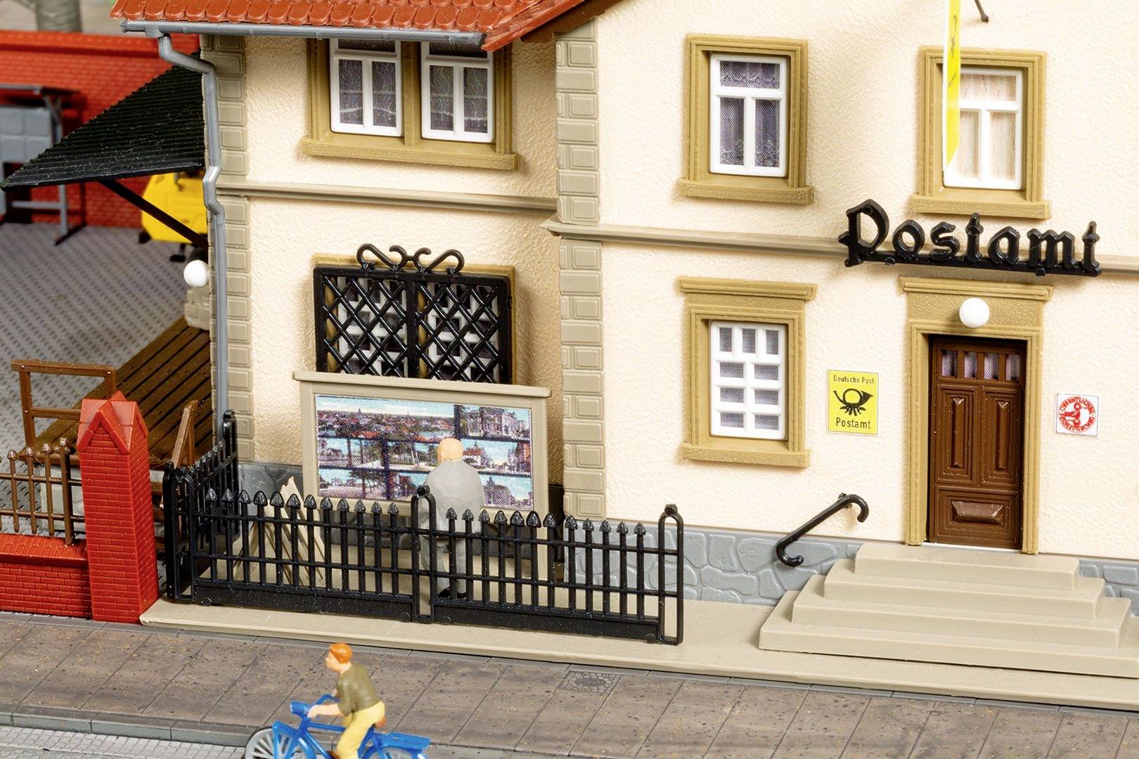 Ein Miniatur-Postamt mit rotem Dach in einem Modellstadt-Diorama, mit einer Figur auf einem Fahrrad im Vordergrund.