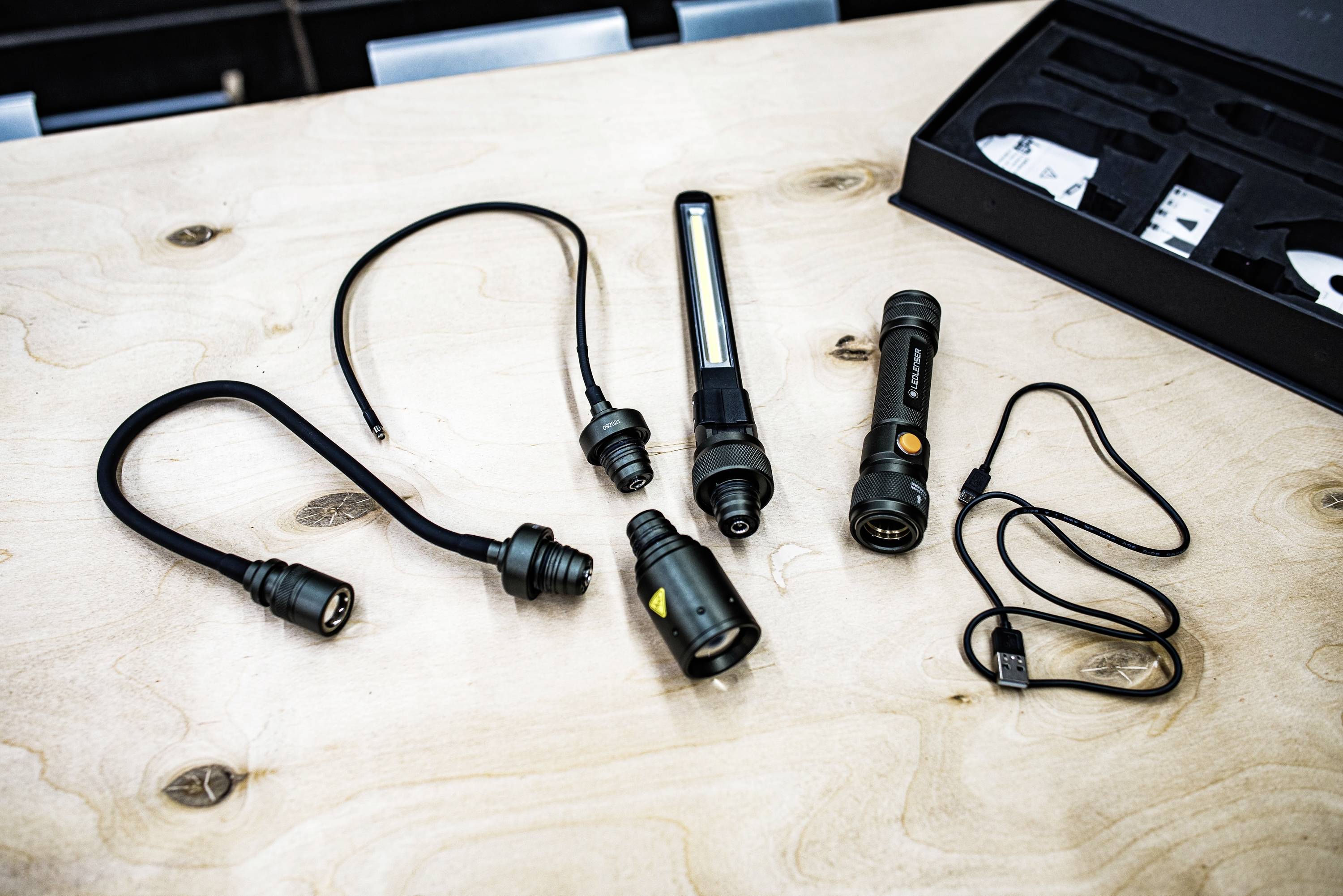 Unterschiedliche Werkzeuge mit Steckern und Kabeln auf einem Holztisch. Links ein flexibles Licht, daneben zwei Handlampen und Zubehör.