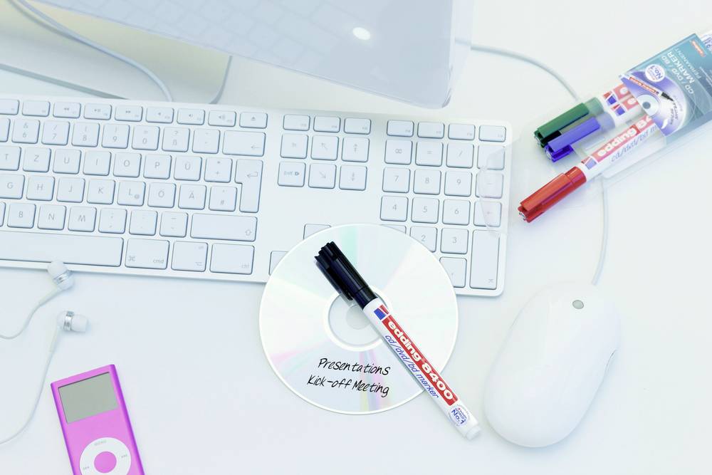 Tastatur und Maus auf Schreibtisch, daneben eine CD mit Beschriftung 'Presentation Kick-off Meeting', Stifte und rosa MP3-Player.