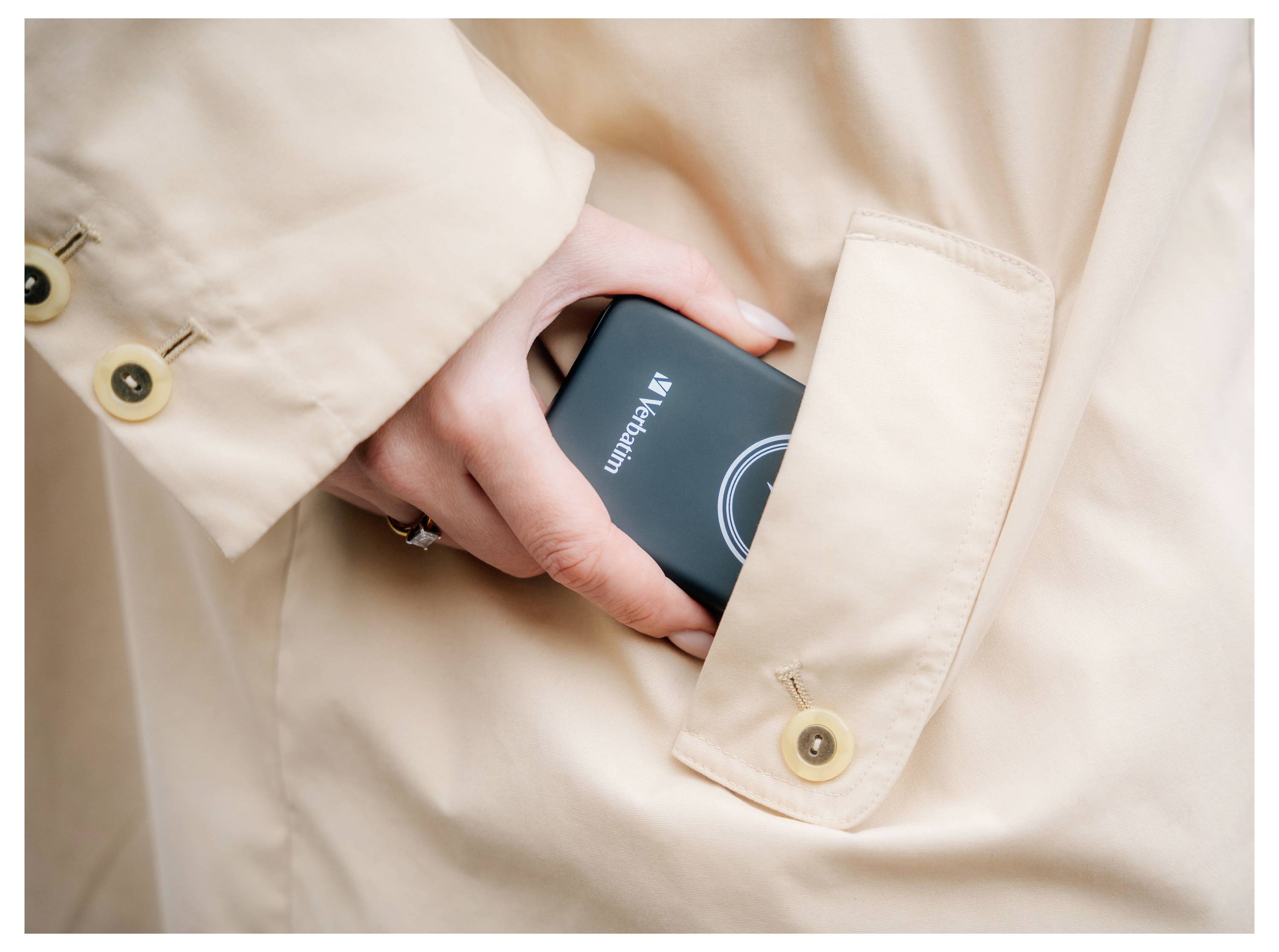 Eine Hand in einem cremefarbenen Mantel steckt eine schwarze tragbare Festplatte der Marke Verbatim in die Tasche.