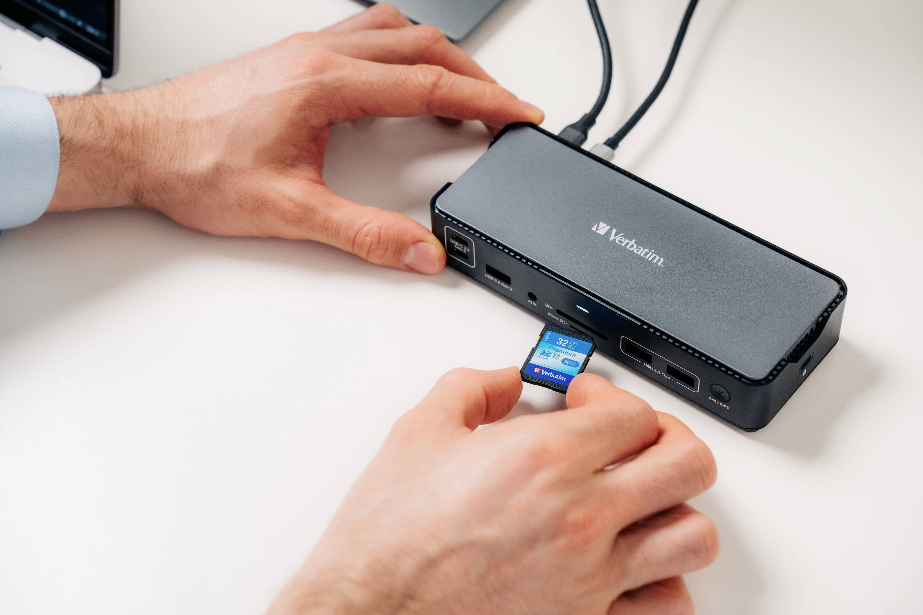 Eine Person steckt eine SD-Karte in ein Verbatim-Multiport-Dockinggerät auf einem Tisch ein.