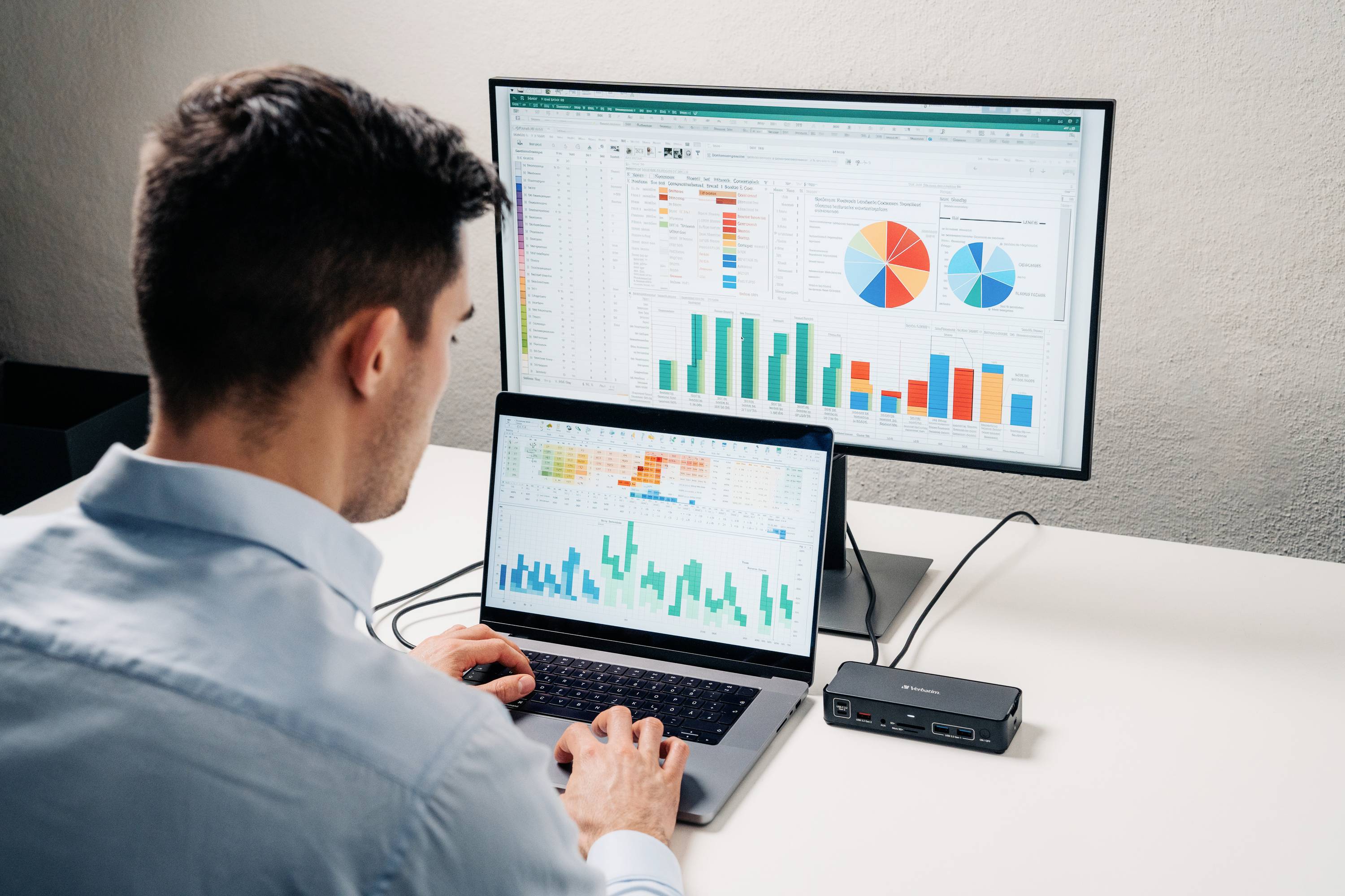 Eine Person arbeitet an einem Laptop, der Diagramme anzeigt, während auf einem zweiten Monitor Diagramme und Tabellen präsentiert werden.