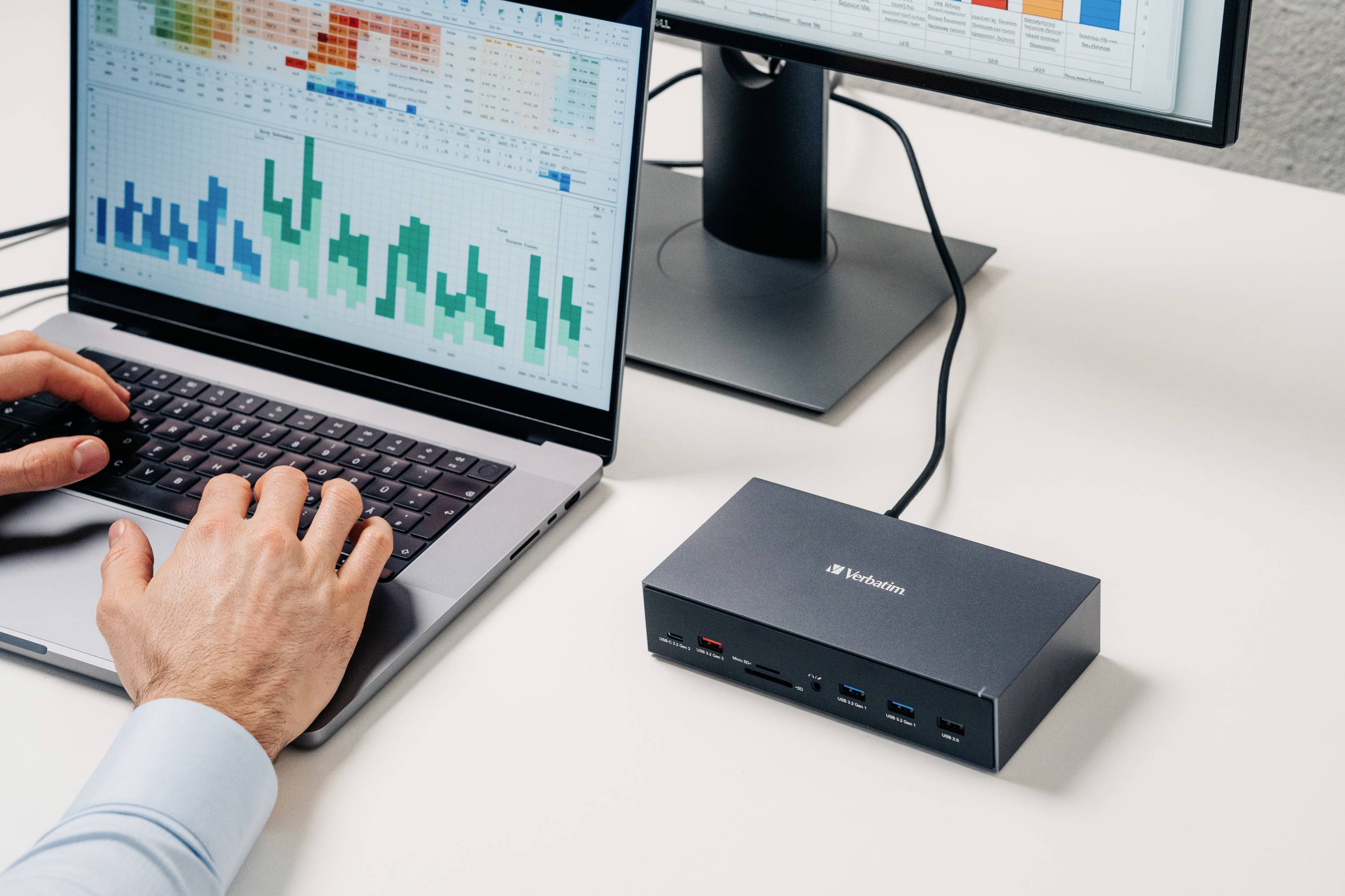 Eine Person arbeitet an einem Laptop, der an eine Dockingstation angeschlossen ist. Auf dem Bildschirm sind farbige Diagramme sichtbar.