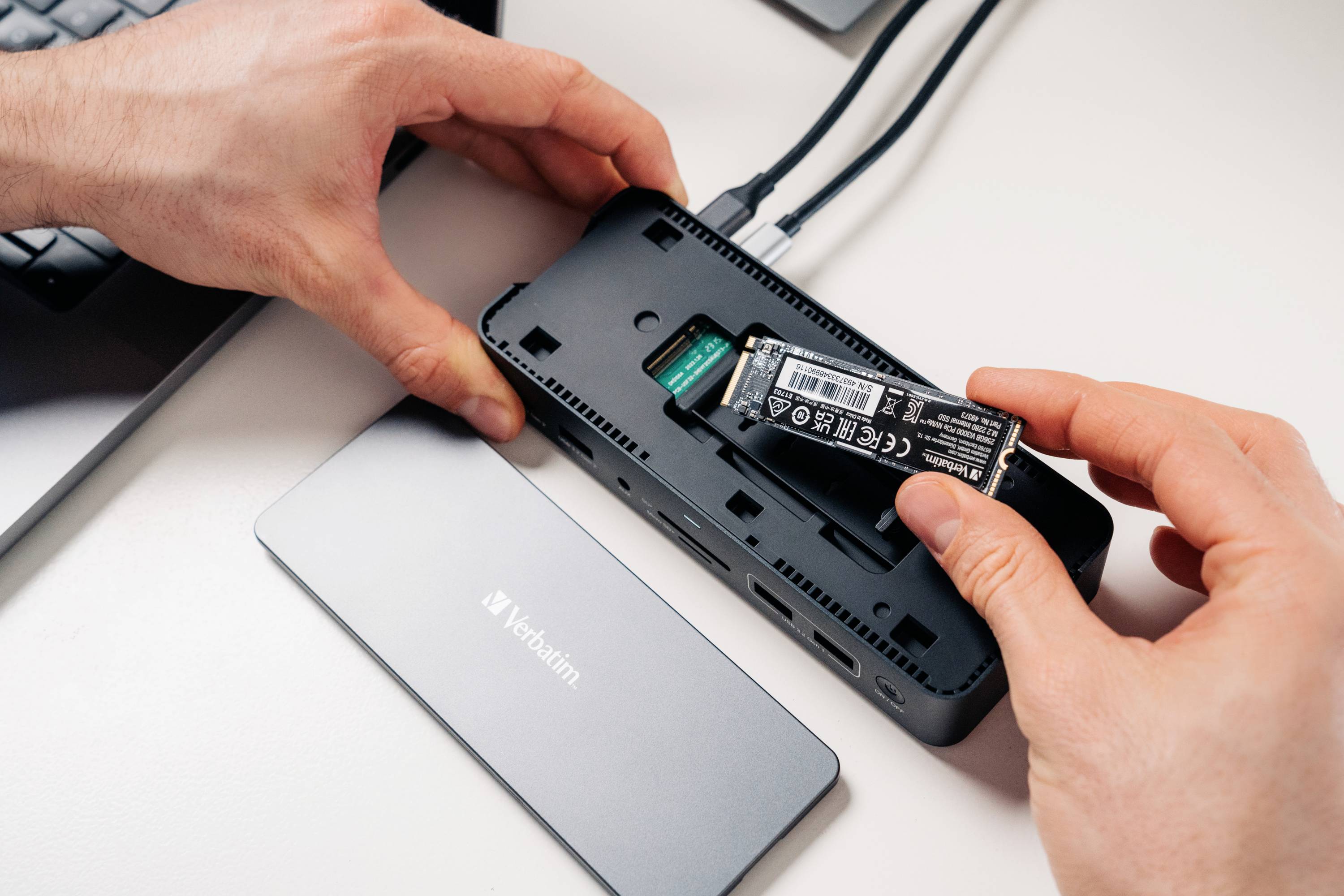 Person installiert eine NVMe SSD in ein externes Gehäuse neben einem Verbatim-Gerät, möglicherweise für erweiterten Speicherplatz.