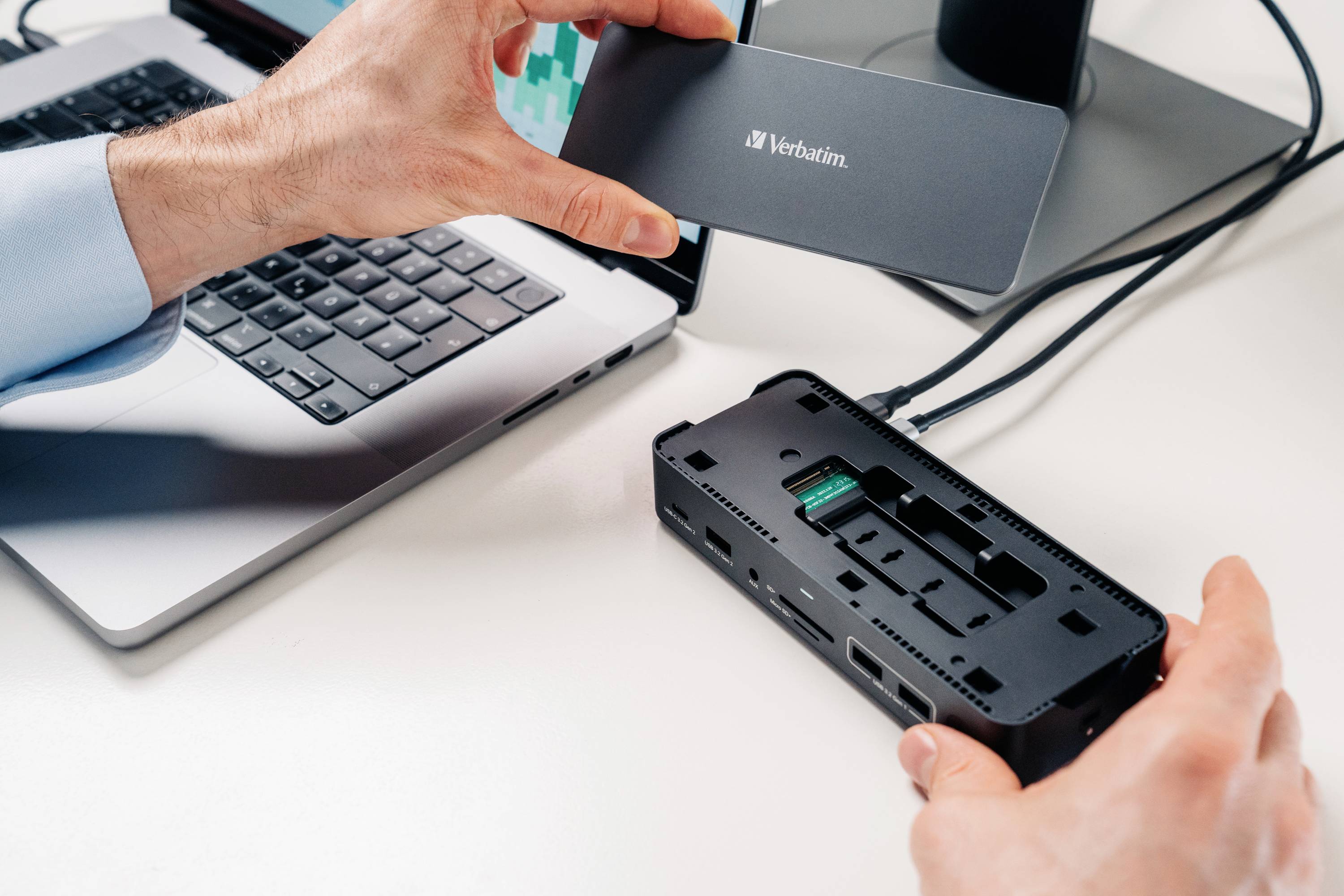 Eine Person verbindet ein Verbatim-Festplattengehäuse mit einem offenen Computer über USB, auf einem Schreibtisch neben einem Laptop.