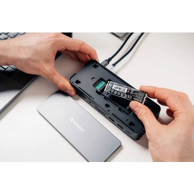Eine Person installiert eine SSD-Festplatte in ein externes Festplattengehäuse auf einem Tisch. Im Hintergrund ist eine Laptop-Tastatur zu sehen.