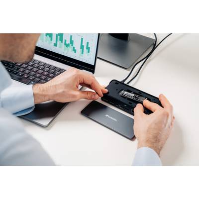 Eine Person installiert eine SSD-Festplatte in ein externes Gehäuse. Im Hintergrund ist ein Laptop mit einem Diagramm auf dem Bildschirm zu sehen.
