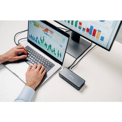 Eine Person arbeitet am Laptop, verbunden mit einem Monitor, der Tabellen mit Diagrammen und Balkendiagrammen zeigt.