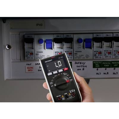 Eine Hand hält ein digitales Multimeter, das 'L0' nahe einer Elektrotafel mit mehreren Sicherungsautomaten zeigt, die mit 'MCB4-125' und 'RCBO40MLH' beschriftet sind.