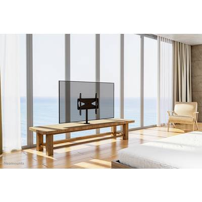 Ein minimalistisch eingerichtetes Wohnzimmer mit großem Fenster und einem Fernseher auf einem Holztisch. Sicht auf das Meer im Hintergrund.