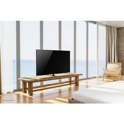 Ein Fernseher steht auf einem Holztisch in einem modernen Raum mit großen Glasfenstern und Blick auf das Meer.