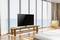 Ein Fernseher steht auf einem Holztisch in einem modernen Raum mit großen Glasfenstern und Blick auf das Meer.