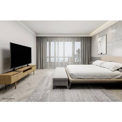 Schlafzimmer mit großem Bett und Flachbildfernseher auf modernem Holzschrank. Große Fenster mit grauen Vorhängen, helle Wände.