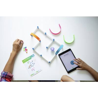 Eine Person konstruiert einen Spielzeugparcours auf einem Tisch. Eine andere Hand nutzt ein Tablet, das scheinbar das Spielzeug steuert.