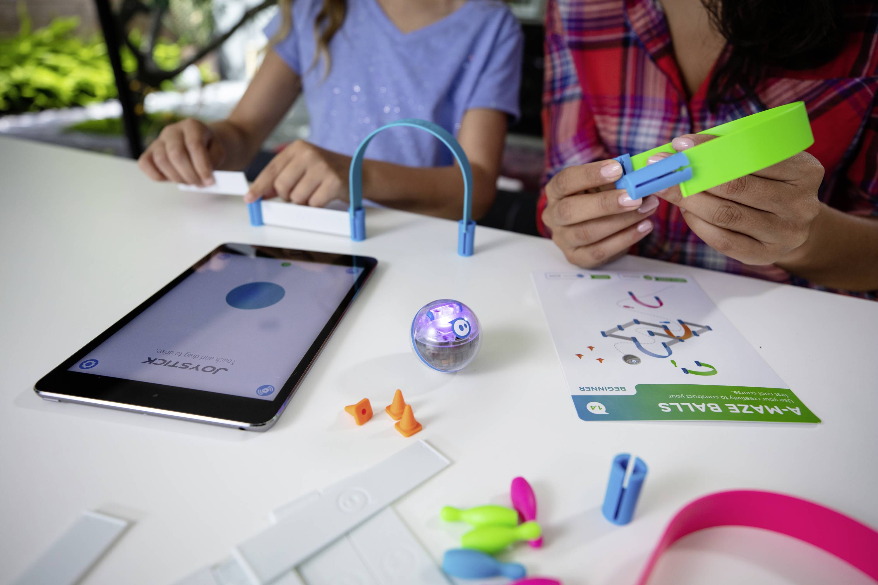 Zwei Personen bauen ein Experiment mit Technik und Spielzeug-Bauteilen. Ein Tablet zeigt eine App an. Kreatives Lernen und Technik.