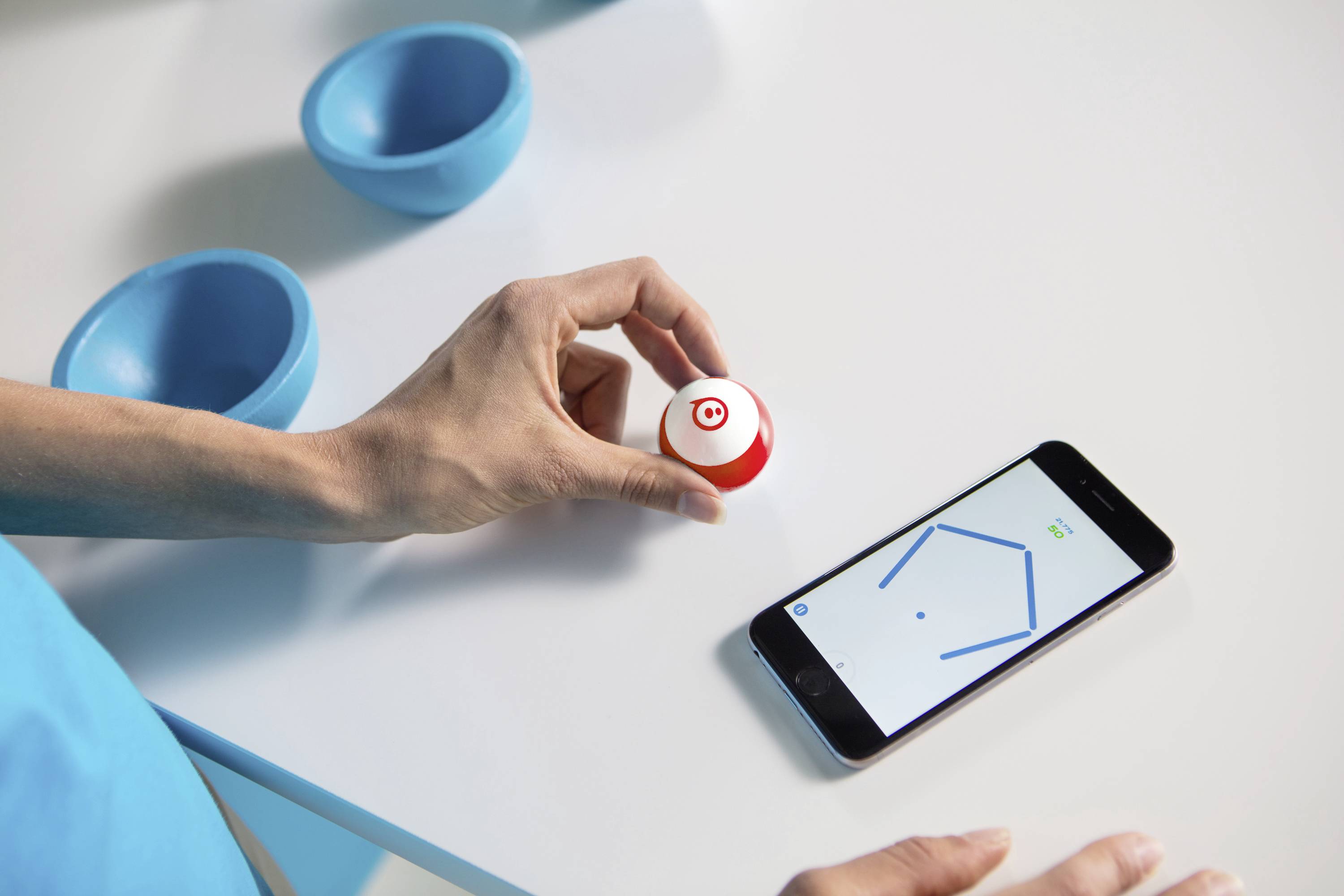 Eine Person hält ein kleines Gerät über einem Smartphone mit einer geöffneten App, die ein geometrisches Muster zeigt.