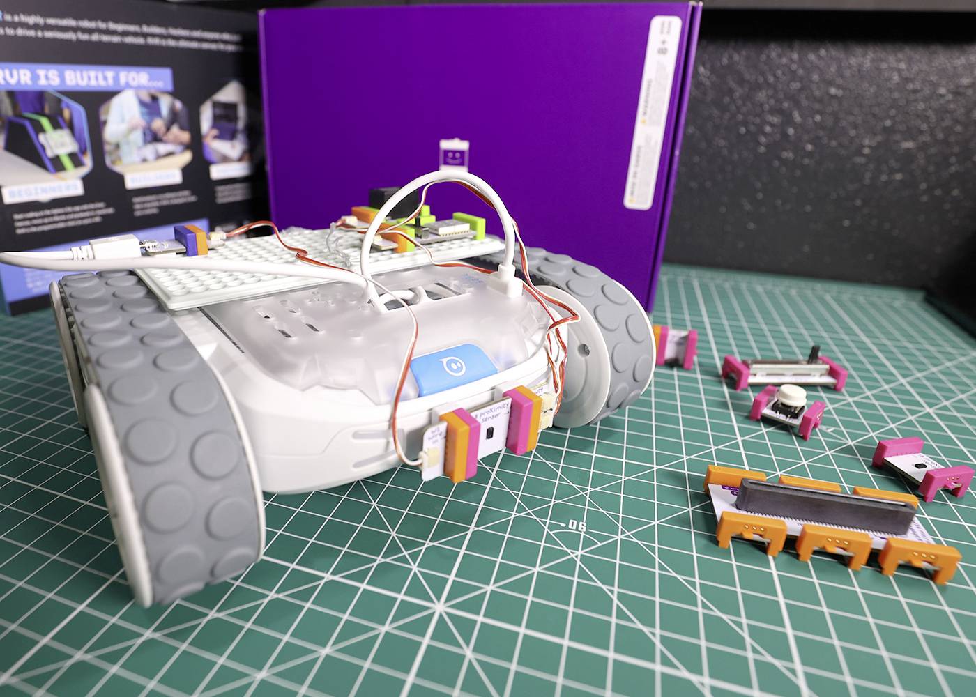 Ein Roboterfahrzeug auf einem Tisch mit elektronischen Bauteilen, umgeben von mehreren kleinen Komponenten, vermutlich im Aufbau oder Test.