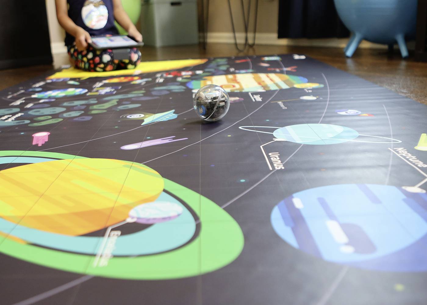 Ein Kind spielt mit einem Roboterball auf einer Matte, die Planeten und das Sonnensystem darstellt. Der Fokus liegt auf Lernen und Spiel.