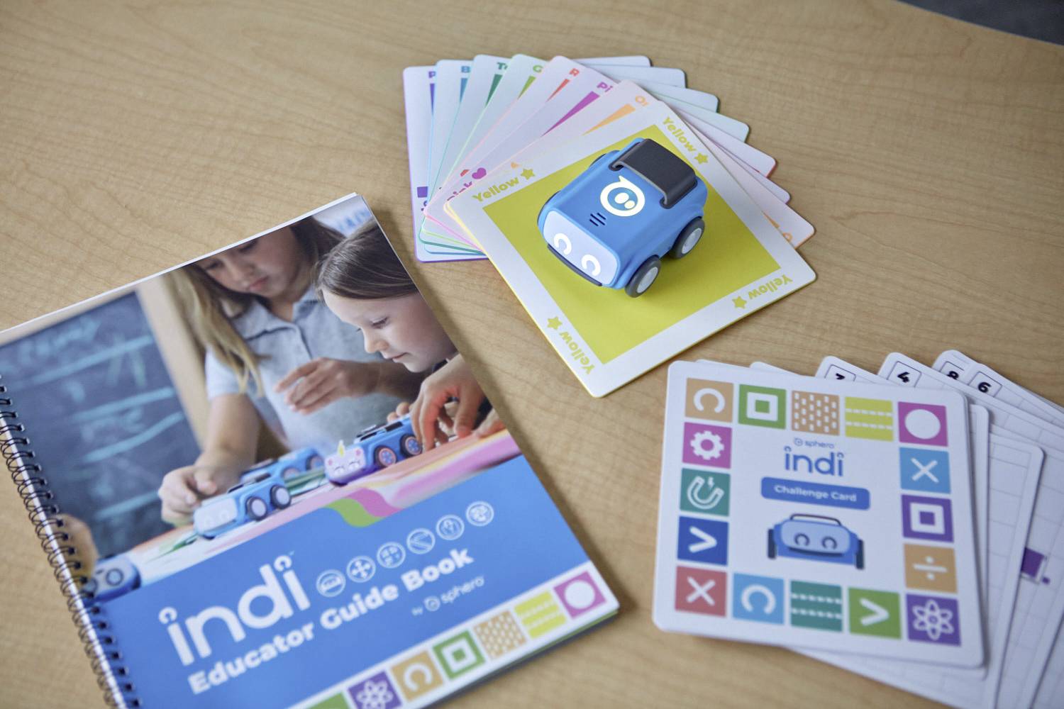 Ein Lehrbuch und Kartenset für den Lernroboter 'indi' zeigen, wie Kinder mit bunten Karten programmieren und Aufgaben lösen können.
