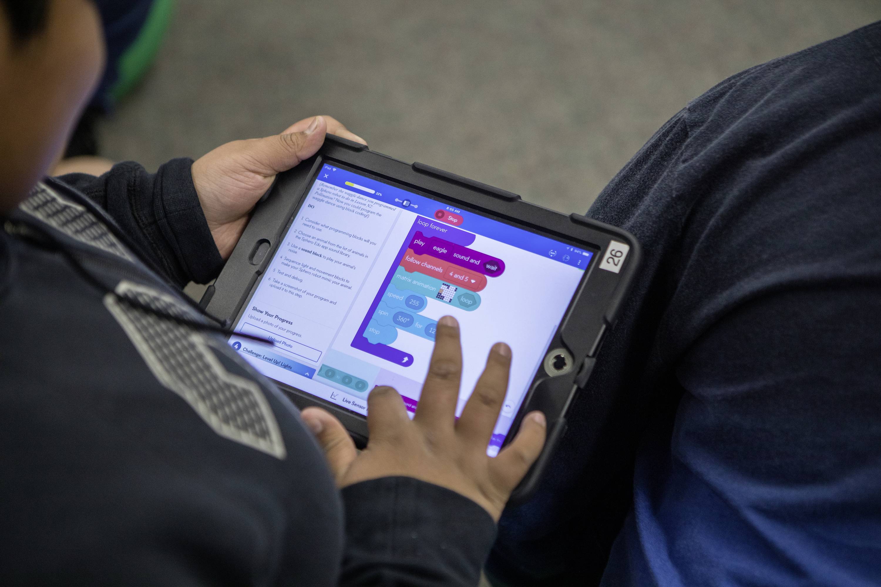 Eine Person nutzt ein Tablet mit einer Programmier-App, um farbige Blöcke zu verbinden, die einem Code ähneln.