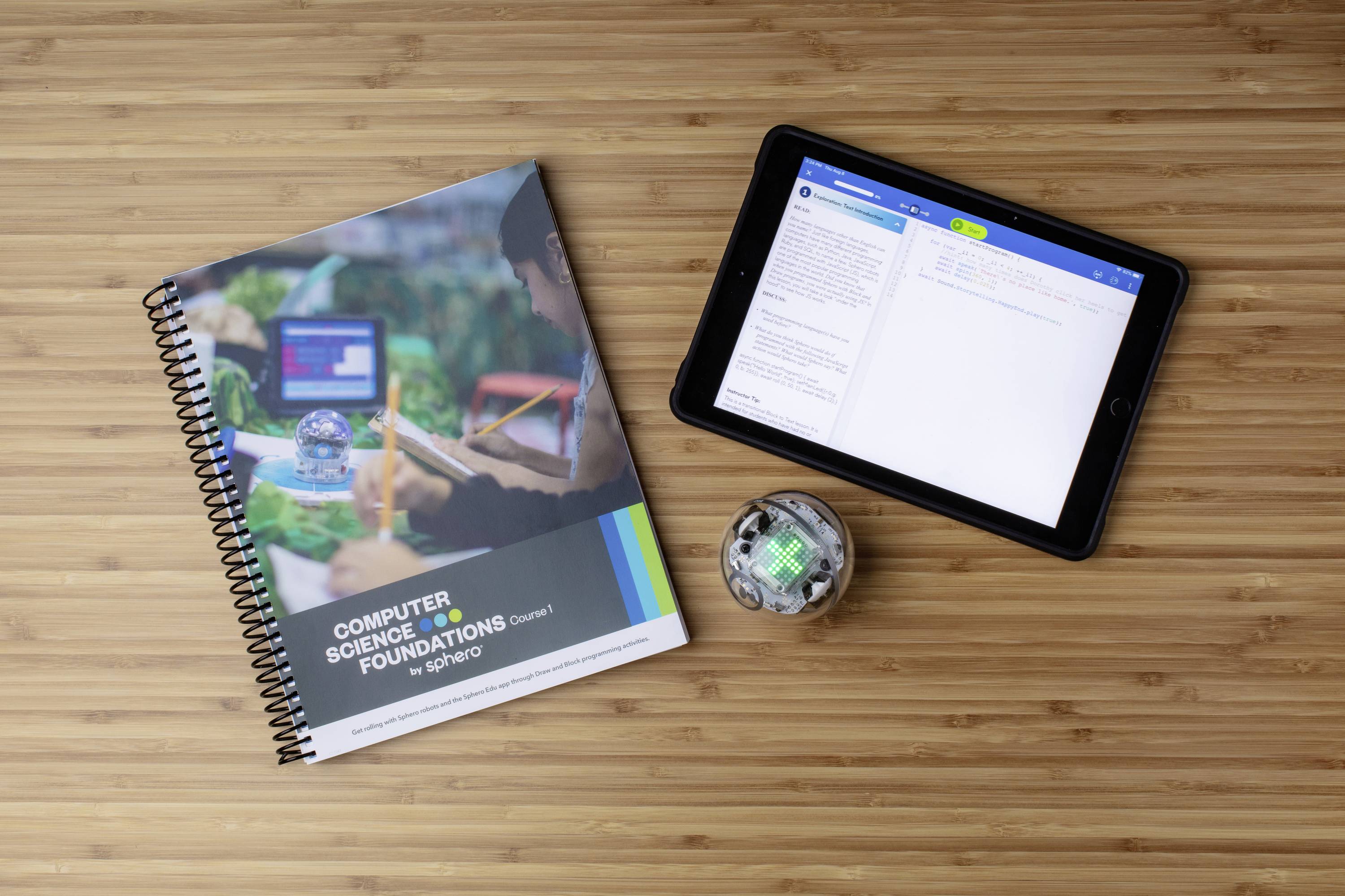 Lehrbuch 'Computer Science Foundations' und ein Tablet, das eine Programmierübung zeigt, liegen auf einem Holztisch neben einem kleinen Roboter.